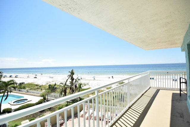 balcony featuring a beach view, a water view, and an in ground hot tub