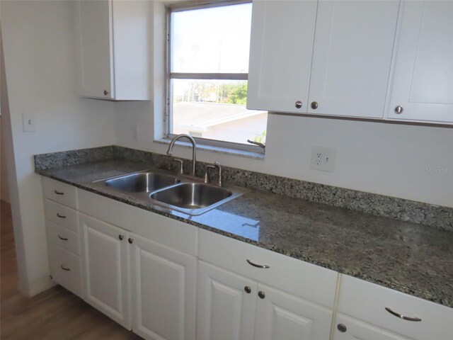 kitchen with white cabinets, hardwood / wood-style flooring, dark stone countertops, and sink