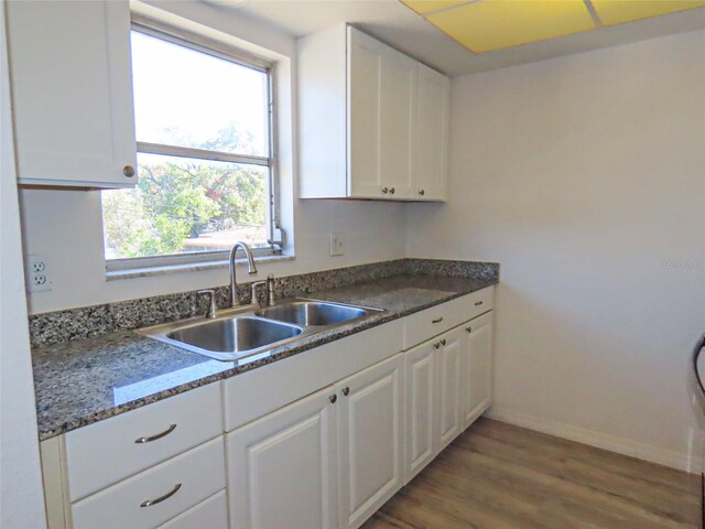 kitchen featuring white cabinets, light wood-type flooring, dark stone counters, and sink