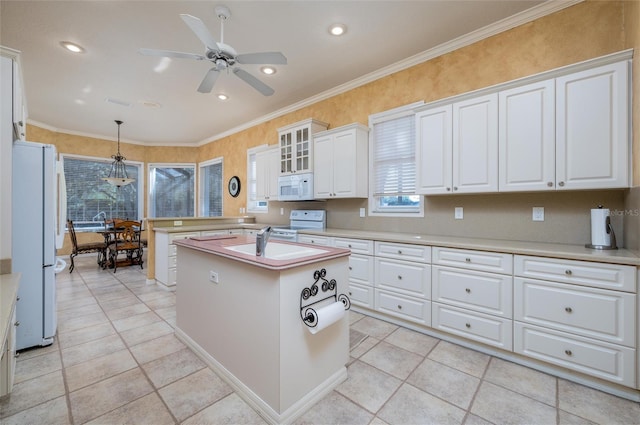 kitchen with white appliances, crown molding, white cabinets, a center island, and hanging light fixtures