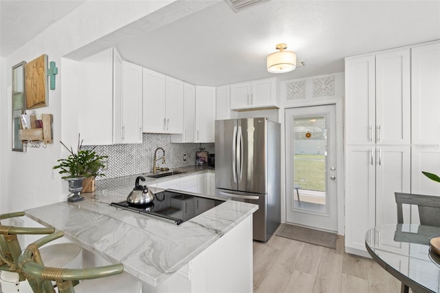 kitchen with light stone countertops, white cabinetry, kitchen peninsula, and stainless steel refrigerator