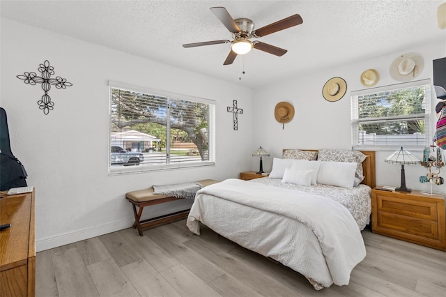 bedroom with ceiling fan, a textured ceiling, light wood-type flooring, and multiple windows