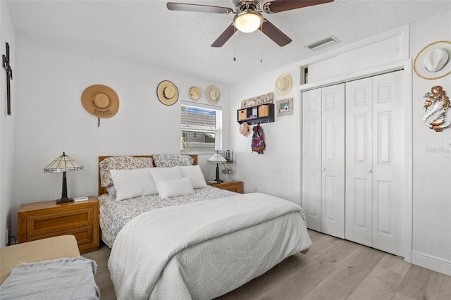 bedroom featuring a closet, light wood-type flooring, ceiling fan, and a textured ceiling