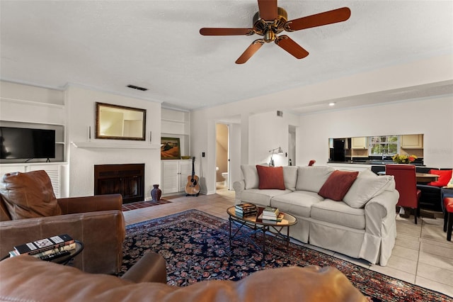 tiled living room with ceiling fan, a textured ceiling, and built in shelves