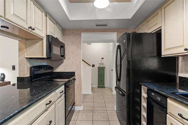 kitchen with light tile patterned floors, black appliances, a raised ceiling, cream cabinetry, and dark stone counters