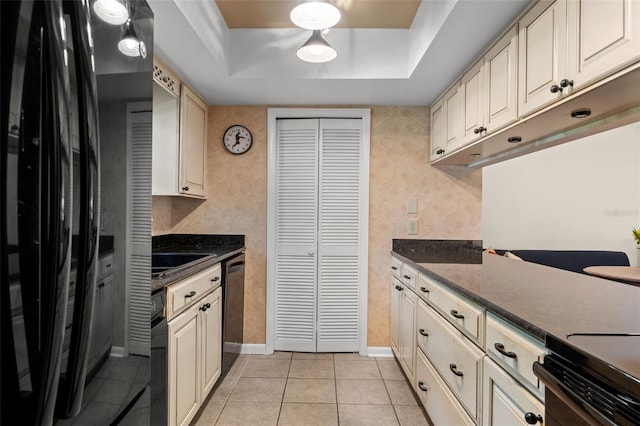 kitchen with light tile patterned flooring, black fridge, a raised ceiling, dishwasher, and cream cabinets