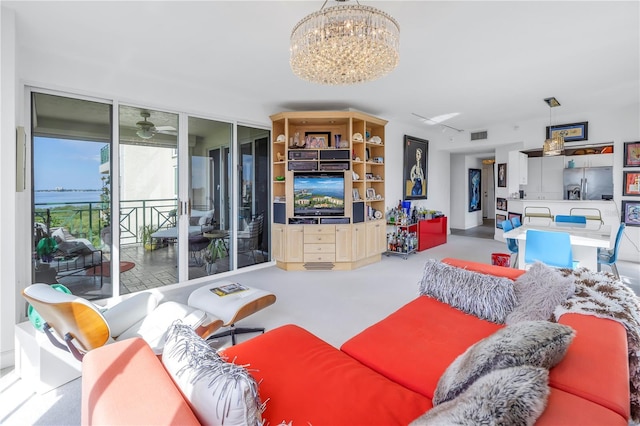 carpeted living room with ceiling fan with notable chandelier and a wall of windows