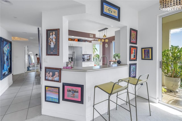 kitchen featuring white cabinets, decorative light fixtures, light tile patterned floors, kitchen peninsula, and stainless steel refrigerator with ice dispenser