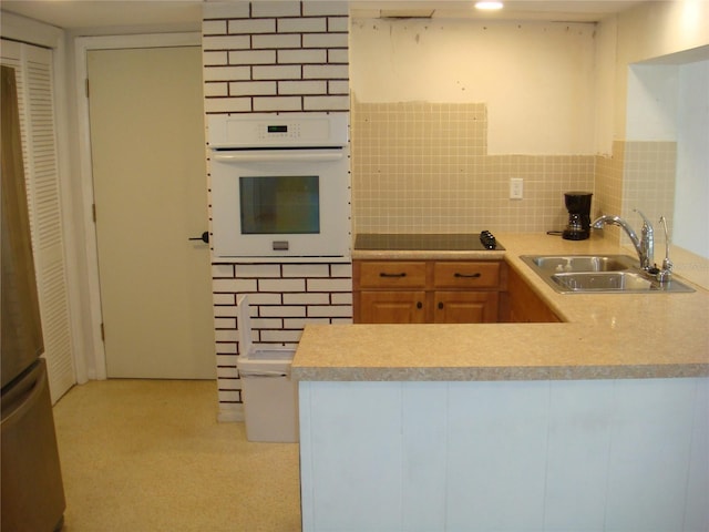 kitchen featuring tasteful backsplash, oven, sink, stainless steel fridge, and black electric cooktop