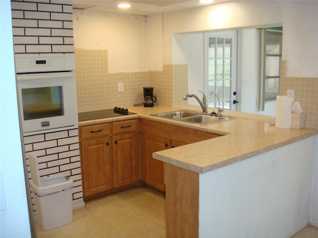 kitchen with backsplash, black electric stovetop, kitchen peninsula, sink, and white oven