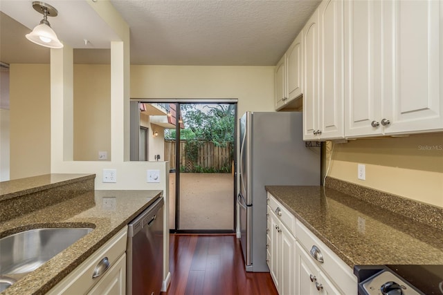 kitchen with dark stone countertops, white cabinets, dark hardwood / wood-style flooring, stainless steel appliances, and decorative light fixtures