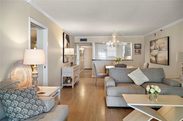 living room featuring wood-type flooring, ornamental molding, a textured ceiling, and a chandelier