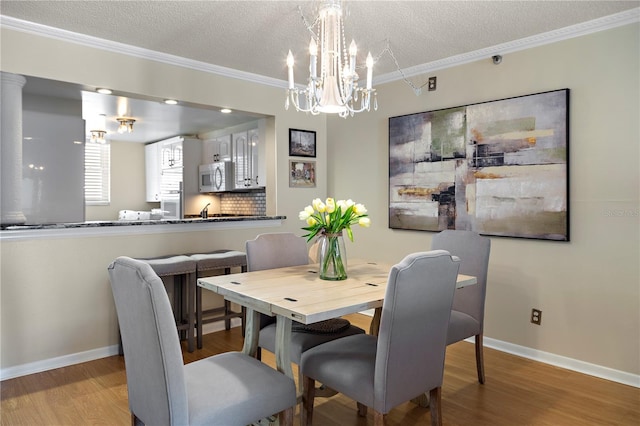 dining space featuring a textured ceiling, crown molding, light hardwood / wood-style flooring, and a notable chandelier