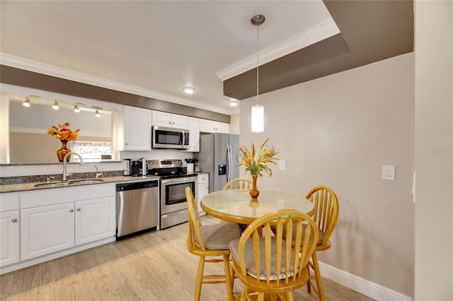 kitchen featuring hanging light fixtures, white cabinets, stainless steel appliances, light wood-type flooring, and sink