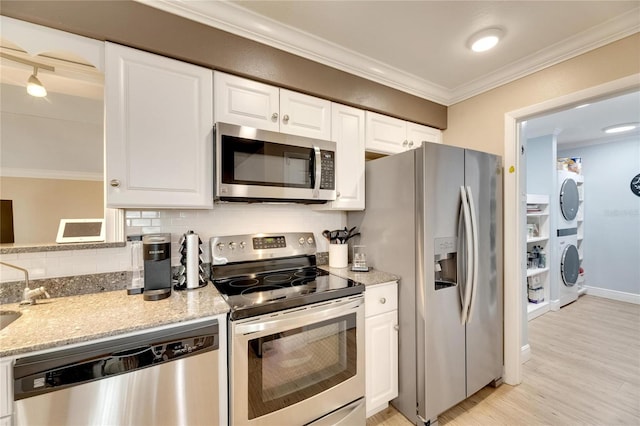 kitchen featuring stainless steel appliances, crown molding, stacked washing maching and dryer, and white cabinetry