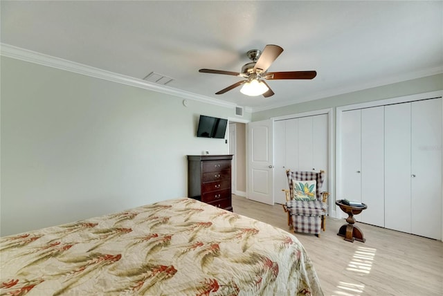 bedroom featuring ceiling fan, multiple closets, light hardwood / wood-style floors, and ornamental molding