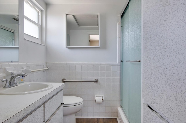 full bathroom with tile walls, hardwood / wood-style floors, bath / shower combo with glass door, vanity, and toilet