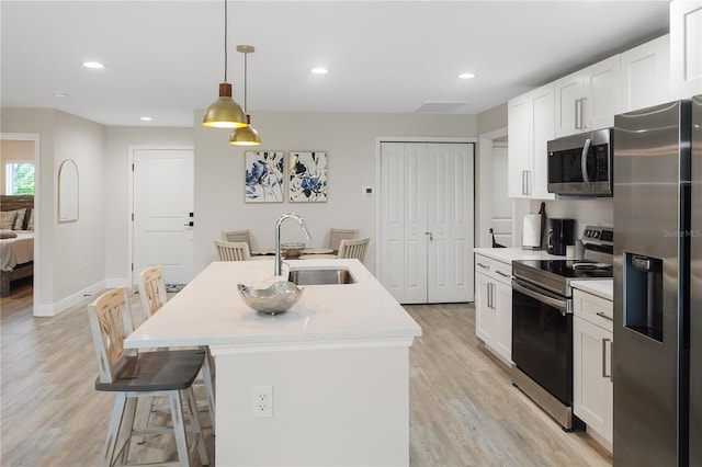 kitchen featuring a kitchen island with sink, white cabinets, sink, appliances with stainless steel finishes, and decorative light fixtures