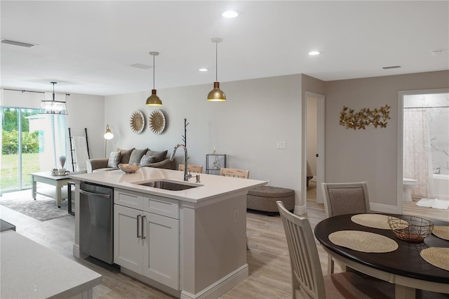 kitchen with an island with sink, sink, light hardwood / wood-style floors, pendant lighting, and dishwasher