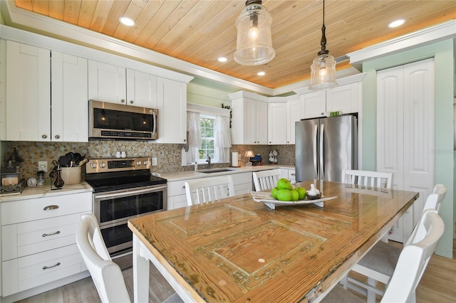 kitchen with light wood-type flooring, white cabinets, hanging light fixtures, a kitchen island, and stainless steel appliances