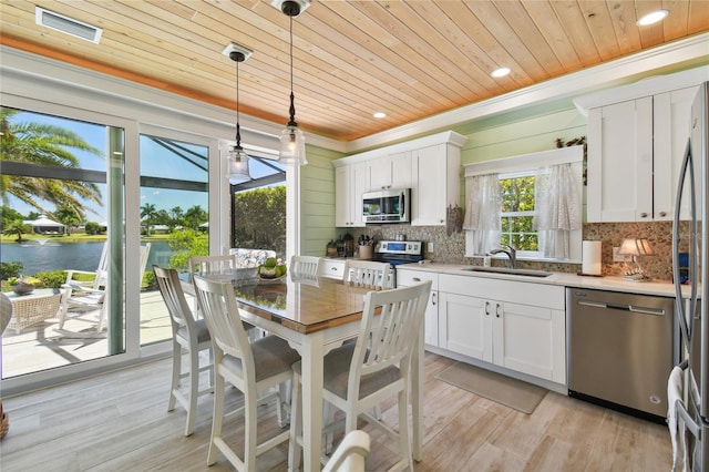 kitchen featuring appliances with stainless steel finishes, a water view, white cabinetry, decorative light fixtures, and sink