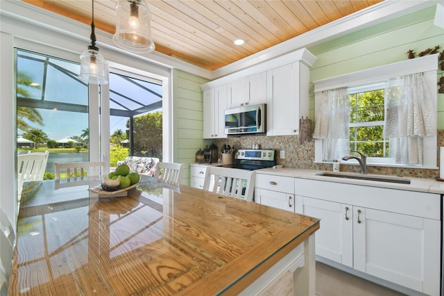 kitchen with wooden walls, white cabinetry, appliances with stainless steel finishes, and sink