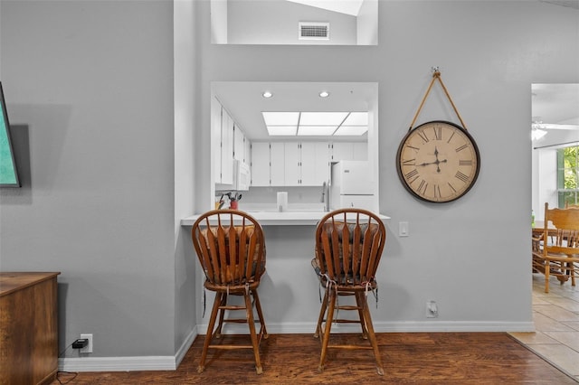 kitchen featuring white cabinets, white appliances, dark hardwood / wood-style flooring, lofted ceiling, and a kitchen bar