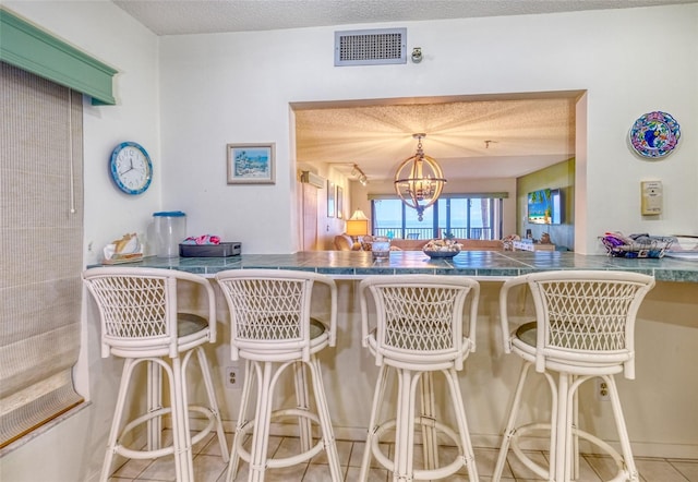 kitchen featuring a notable chandelier, tile patterned floors, a textured ceiling, and a kitchen breakfast bar