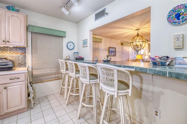 kitchen with tasteful backsplash, a textured ceiling, a notable chandelier, light tile patterned floors, and light brown cabinets