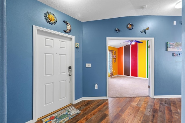 entrance foyer with a textured ceiling, vaulted ceiling, ceiling fan, and dark wood-type flooring