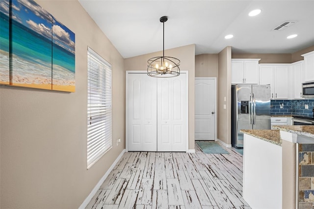 kitchen with light stone counters, lofted ceiling, white cabinetry, decorative backsplash, and stainless steel appliances