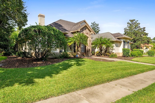 view of front facade with a chimney, a shingled roof, stucco siding, and a front lawn