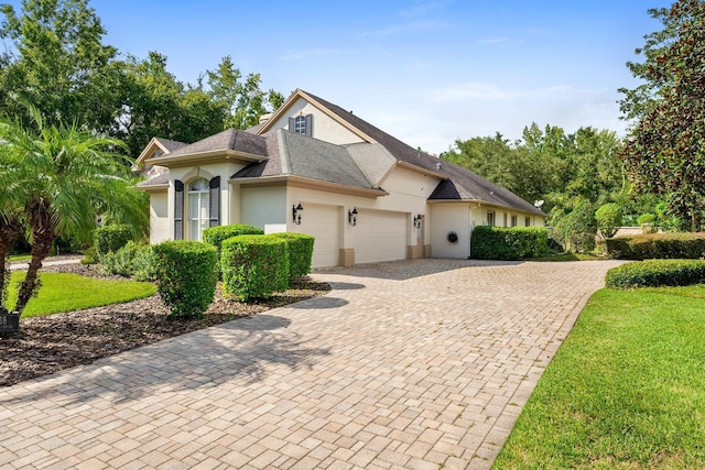 view of front of property with a front lawn, decorative driveway, stucco siding, and an attached garage