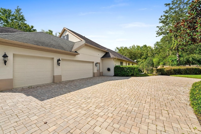 view of property exterior featuring stucco siding, an attached garage, roof with shingles, and decorative driveway