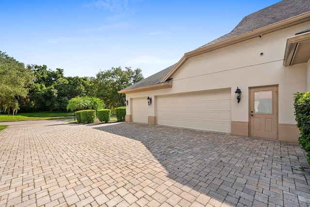 view of side of home featuring decorative driveway, a garage, and stucco siding