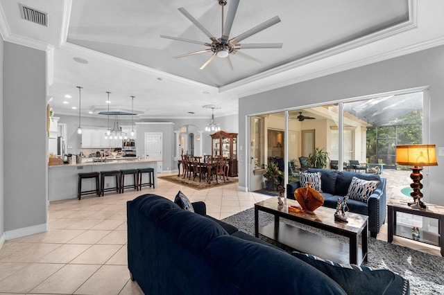 living area featuring a raised ceiling, light tile patterned flooring, ceiling fan with notable chandelier, and visible vents
