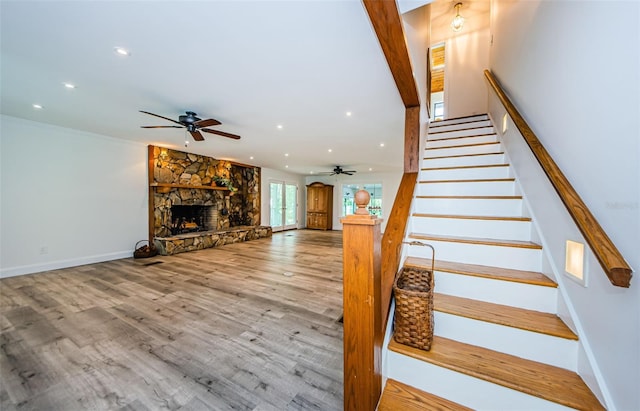 stairs featuring wood-type flooring, a stone fireplace, and ceiling fan