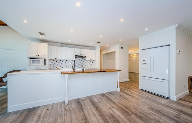 kitchen featuring light hardwood / wood-style flooring, backsplash, a spacious island, white appliances, and white cabinets