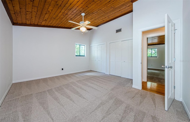 unfurnished bedroom with multiple closets, ceiling fan, light colored carpet, and wooden ceiling