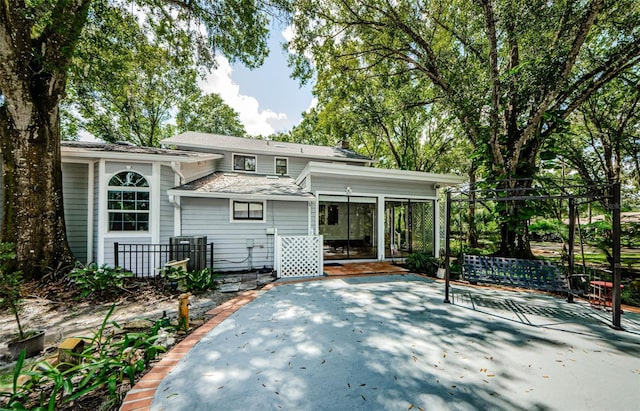 rear view of property featuring a patio area, a sunroom, and a shingled roof