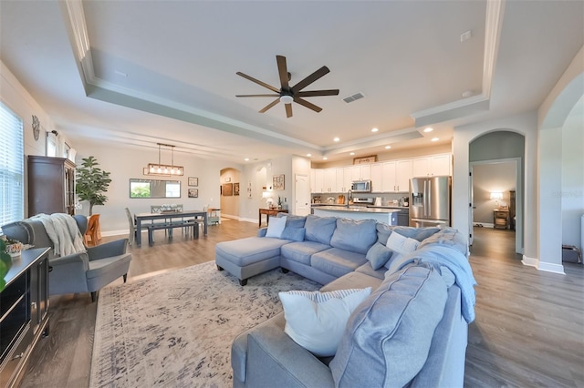 living room with ceiling fan, a raised ceiling, crown molding, and dark wood-type flooring