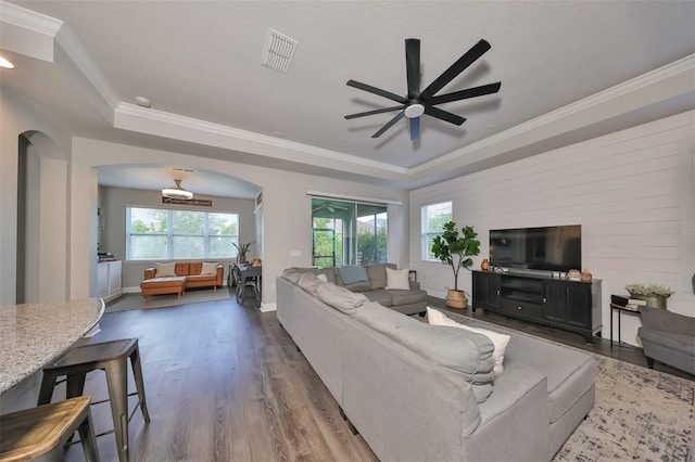 living room with wood-type flooring, a raised ceiling, ornamental molding, and ceiling fan