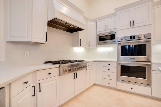 kitchen featuring tasteful backsplash, custom range hood, appliances with stainless steel finishes, light countertops, and white cabinetry