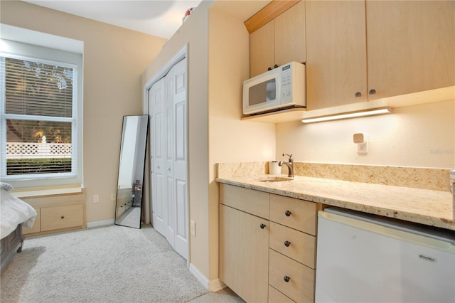 kitchen featuring white appliances, light brown cabinets, light stone countertops, a sink, and light colored carpet