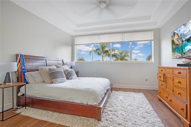 bedroom with a tray ceiling, wood finished floors, and baseboards