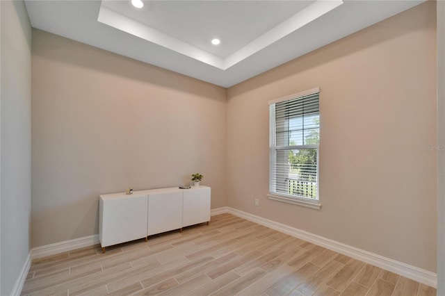 empty room featuring light wood-type flooring and a raised ceiling