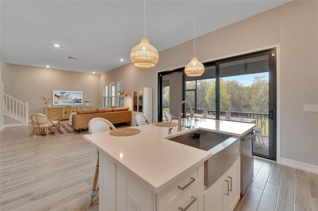 kitchen with dishwasher, an island with sink, white cabinetry, light hardwood / wood-style flooring, and decorative light fixtures