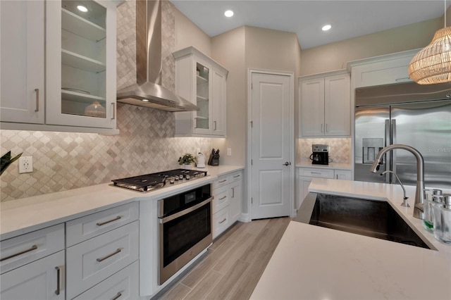 kitchen with appliances with stainless steel finishes, hanging light fixtures, white cabinetry, sink, and wall chimney range hood