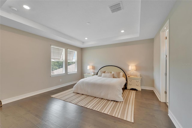 bedroom featuring a raised ceiling and dark hardwood / wood-style flooring