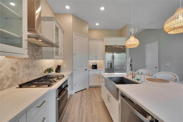 kitchen featuring appliances with stainless steel finishes, hanging light fixtures, white cabinets, wall chimney exhaust hood, and sink